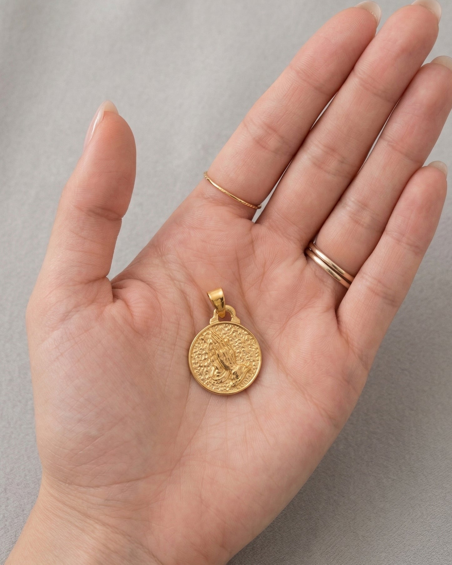 Dije de medalla circular dorada con grabado de manos en oración