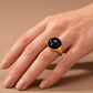 Anillo dorado con piedra de gota color negro, de tipo ajustable.
