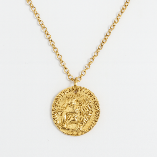 Collar dorado con cadena delgada y dije tipo moneda antigua, con relieve de perfil clásico y detalles en bajo relieve alrededor. Su diseño clásico y elegante es ideal para elevar cualquier look minimalista con un toque sofisticado y atemporal.